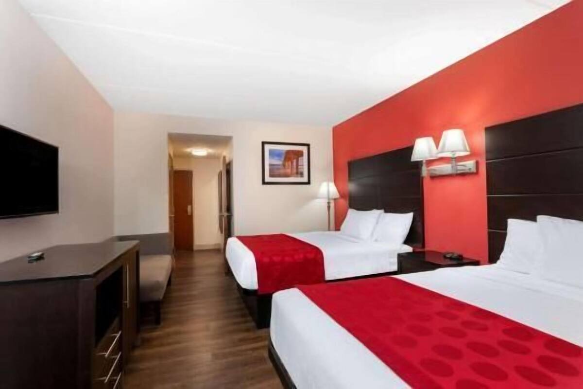 A hotel room with two beds, a TV, a desk, and a door leading to another room.