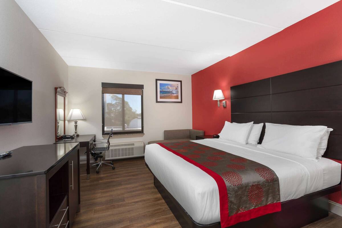 A hotel room with a bed, desk, chair, and a TV.