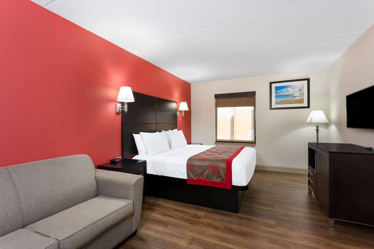 A hotel room with a bed, a grey sofa, a TV, and a desk.