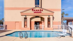 Un edificio con un cartel que dice "RAMADA BY WYNDHAM" y una piscina delantera.
