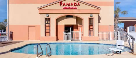 Un edificio con un cartel que dice "RAMADA BY WYNDHAM" y una piscina delantera.
