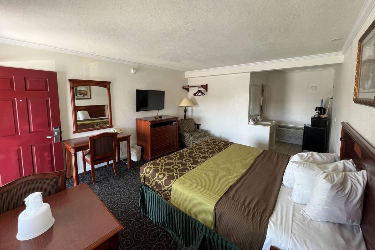 A hotel room with a bed, a desk, a chair, a TV, a mirror, and a bathroom.