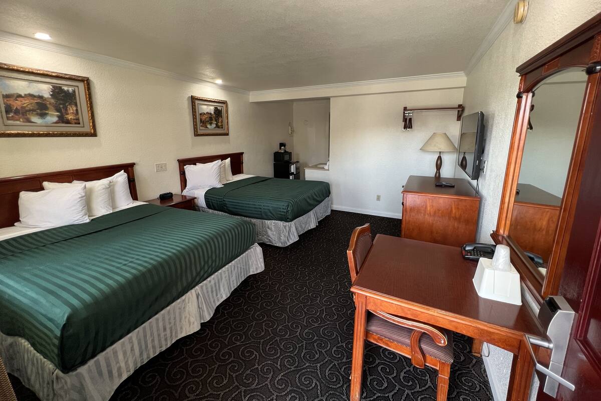 A hotel room with two beds, a desk, a chair, a dresser, a mirror, and a television.
