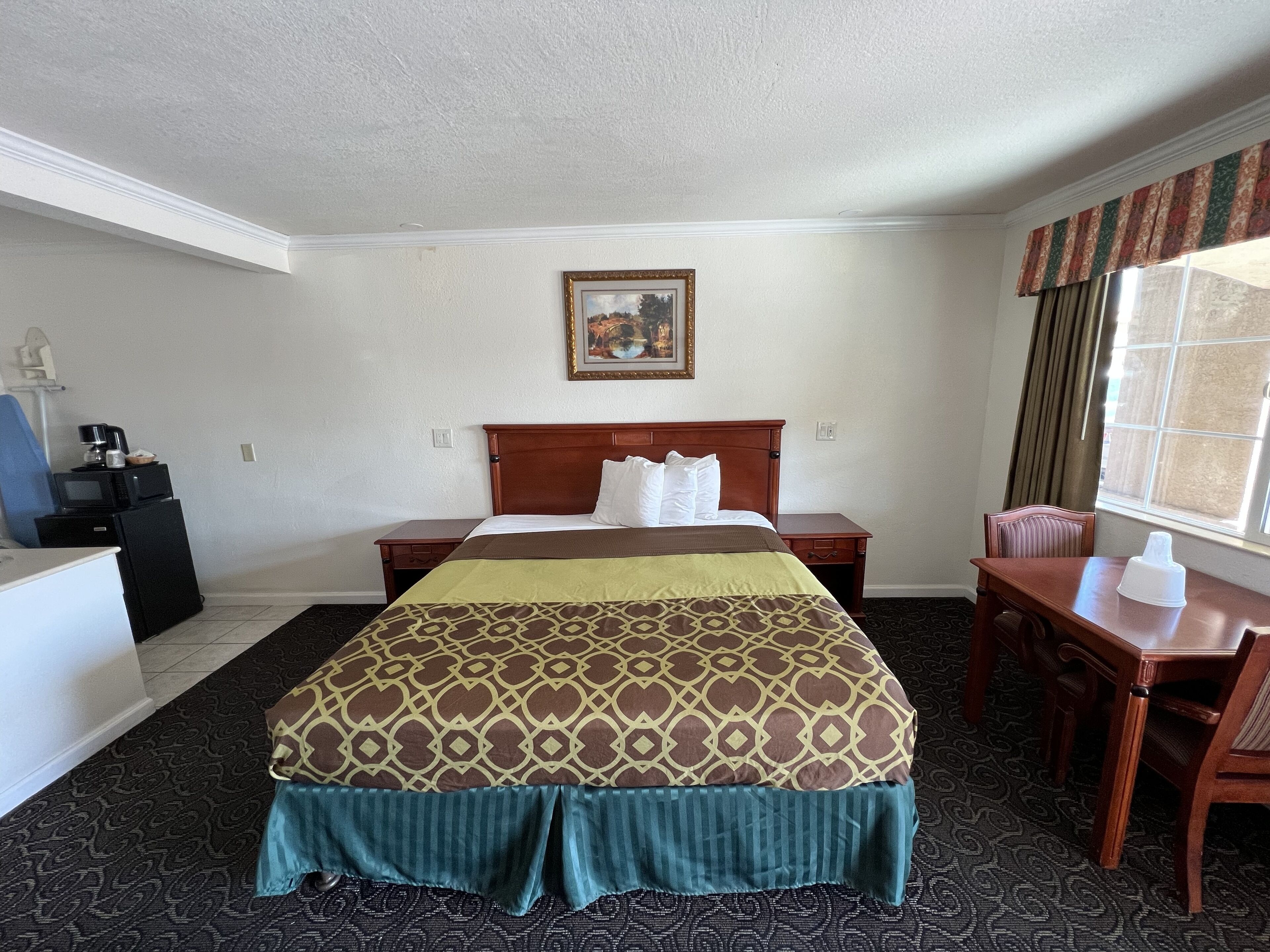 Hotelkamer met een groot bed, een bureau, een stoel, een tafeltje, een magnetron, een koelkast en een raam met gordijnen.
