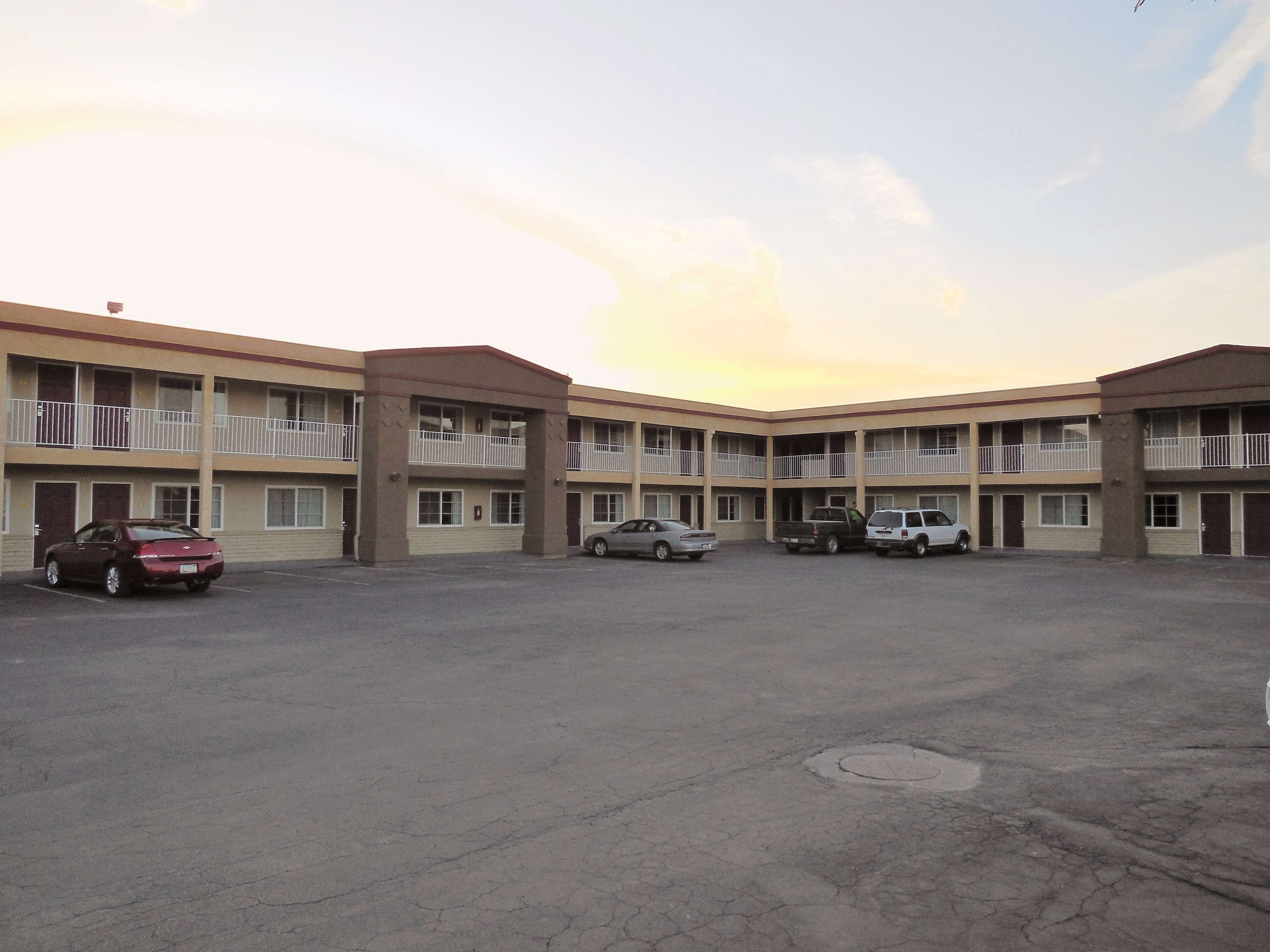 A multi-story motel with a central courtyard, featuring a row of parking spaces and a few parked cars.