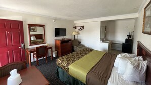 A hotel room with a bed, a desk, a chair, a television, a mirror, and a bathroom visible through an open door. - Americas Best Value Inn Hanford (Hanford)