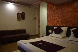 A hotel room with a bed, a sofa, a wall-mounted clock, and a thermostat.