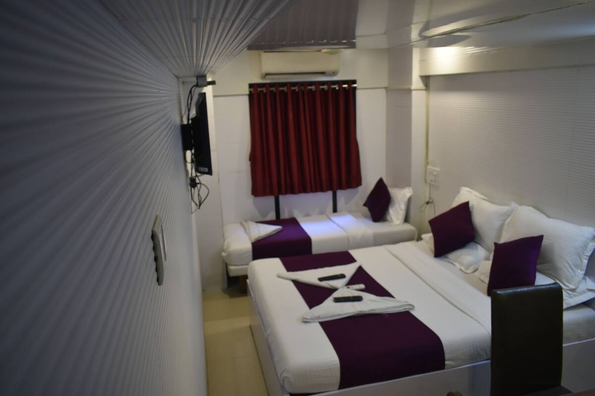 Quarto de hotel com duas camas, uma cortina vermelha e uma parede branca com televisão fixada.