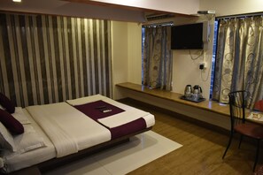 A hotel room with a bed, a TV mounted on the wall, a desk with a chair, and a window with curtains.