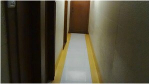 Un pasillo estrecho con suelo a rayas amarillo y blanco, una puerta de madera al final y paredes lisas.
