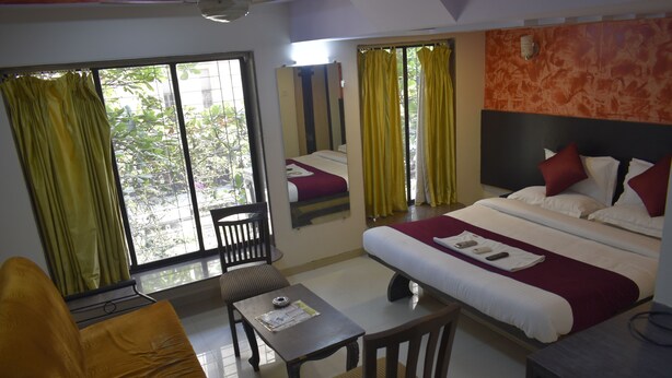 Una habitación de hotel con cama, escritorio, silla y ventana con cortinas.