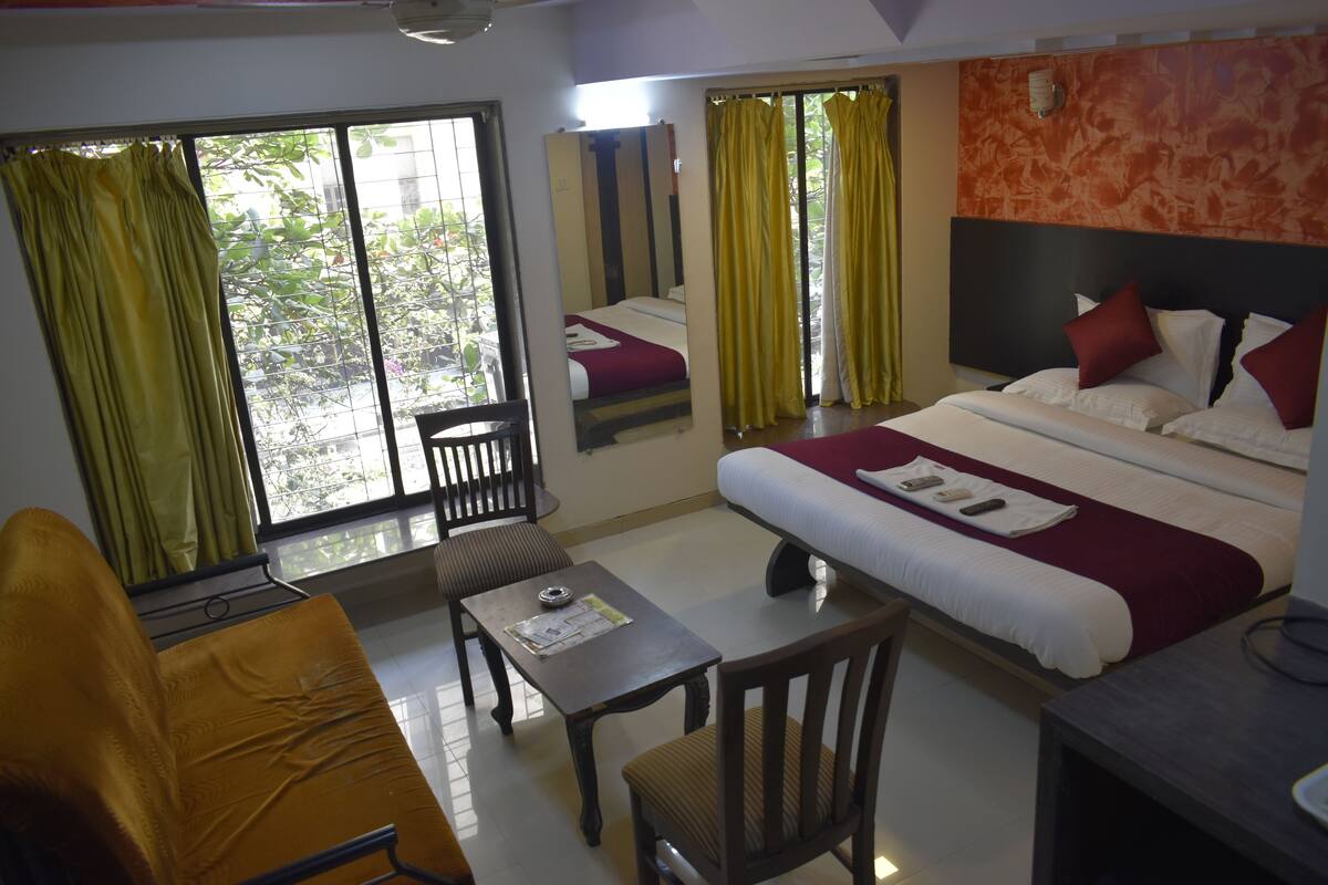 Quarto de hotel com cama, escrivaninha, cadeira e janela com cortinas.