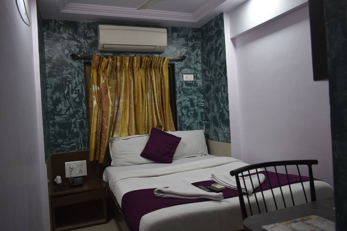 Quarto de hotel com cama, mesa de cabeceira, cadeira e aparelho de ar condicionado.