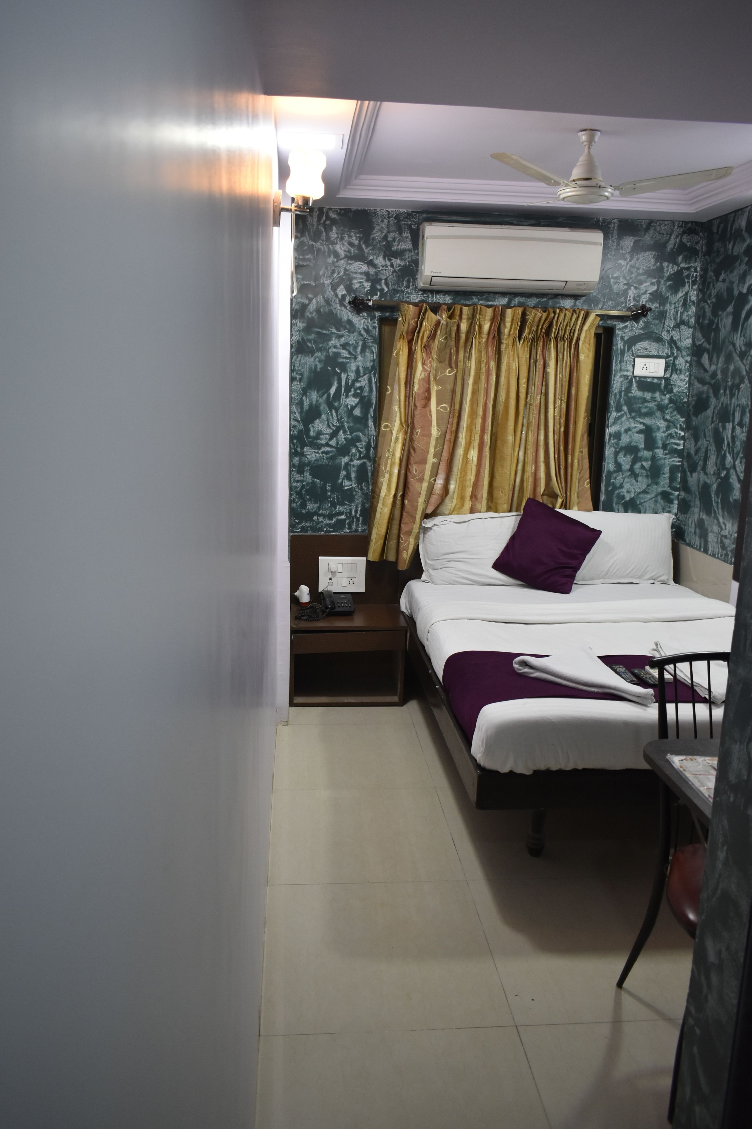 A hotel room with a bed, a nightstand, an air conditioning unit, and a ceiling fan.