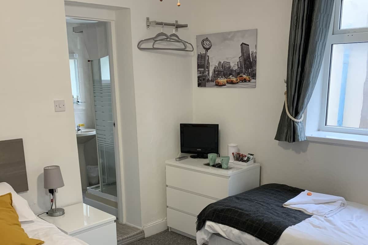 A hotel room with two beds, a desk, a television, a painting, and a window with curtains.