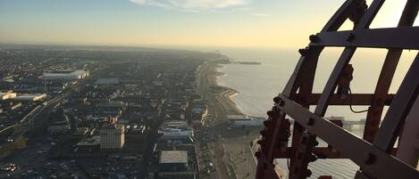 An aerial view of a coastal city with a prominent Ferris wheel, a large stadium, and a beach in the distance.
