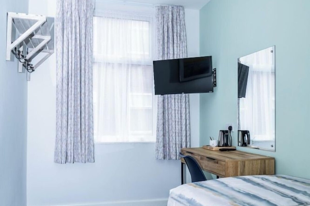 A hotel room with a bed, a desk, a chair, a television, and a window with curtains.