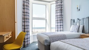 A hotel room with two beds, a desk, a chair, and a view of the beach. - The Craig-Y-Don Hotel (Blackpool)