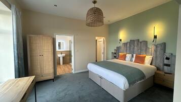 A bedroom with a large bed, a wooden desk, a wardrobe, and a bathroom visible through an open door.
