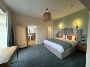 A bedroom with a large bed, a wooden desk, a wardrobe, and a bathroom visible through an open door. - The Craig-Y-Don Hotel (Blackpool)