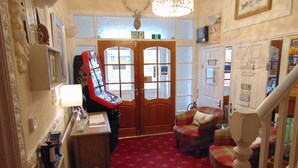 A cozy room with a red carpet, a wooden desk with a lamp, a plaid armchair, and a staircase with a white balustrade. - The Golden Sands (Blackpool)