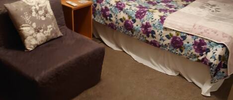 Une chambre à coucher avec un lit, une chaise, une table de chevet et une lampe.