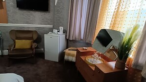 A hotel room with a flat-screen TV mounted on the wall, a sofa, a small table with a plant, and a bed. - The Golden Sands (Blackpool)
