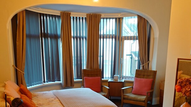 A hotel room with a large bed, two chairs, a small table, and a dresser. - The Golden Sands (Blackpool)