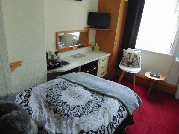 A hotel room with a bed, a desk with a computer, a chair, a small table, and a television on the wall. - The Golden Sands (Blackpool)