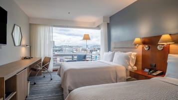 A hotel room with two beds, a desk, a chair, a phone, and a view of the city.