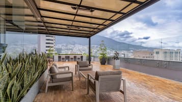 A rooftop terrace with outdoor seating, potted plants, and a view of the city and mountains.