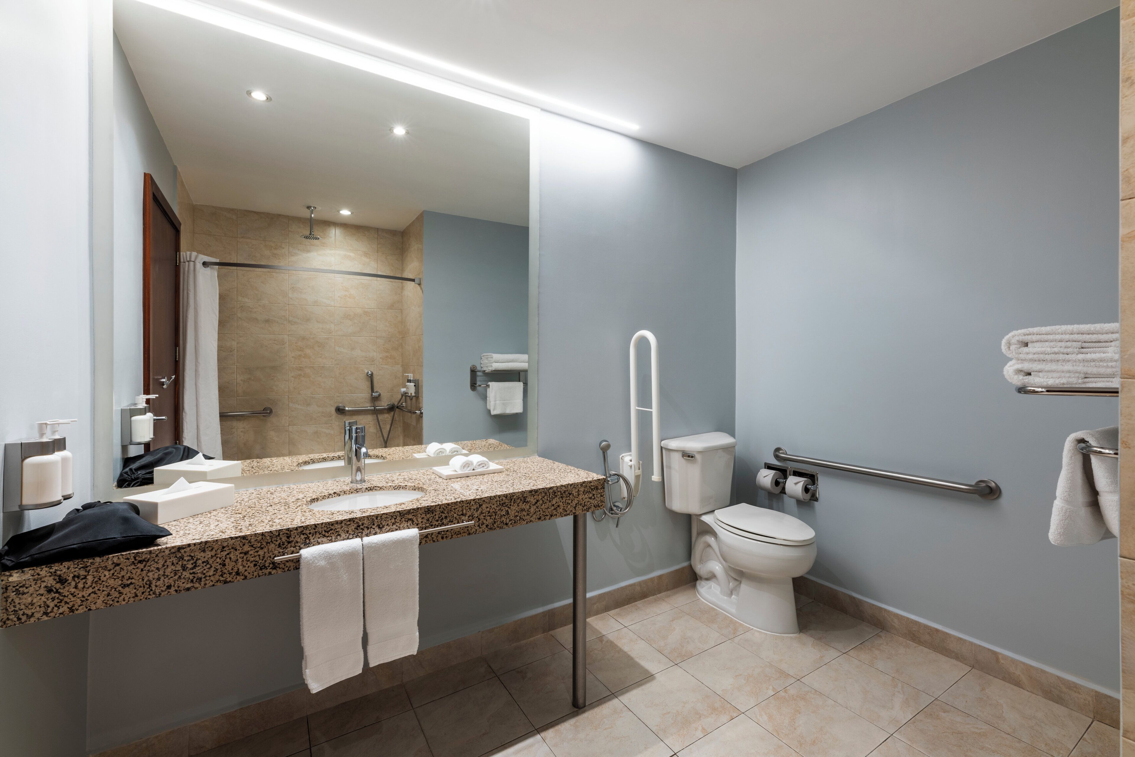 A modern bathroom with a granite countertop sink, a mirror, a toilet, and a shower area.