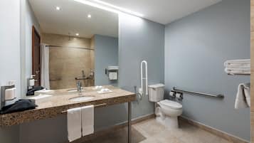 A modern bathroom with a granite countertop sink, a mirror, a toilet, and a shower area.