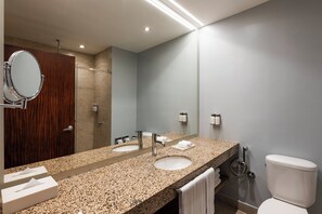 A modern bathroom with a granite countertop, two sinks, a large mirror, a toilet, and a shower area.