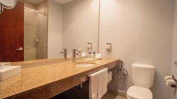 A modern bathroom with a granite countertop, two sinks, a large mirror, and a toilet.
