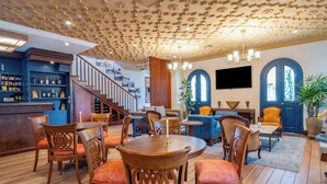 Un salón amplio con suelo de madera, una escalera y una zona de bar con estantes llenos de botellas.