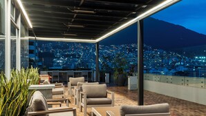 Zona de estar al aire libre con sillas y mesas, con vistas a un paisaje urbano nocturno.