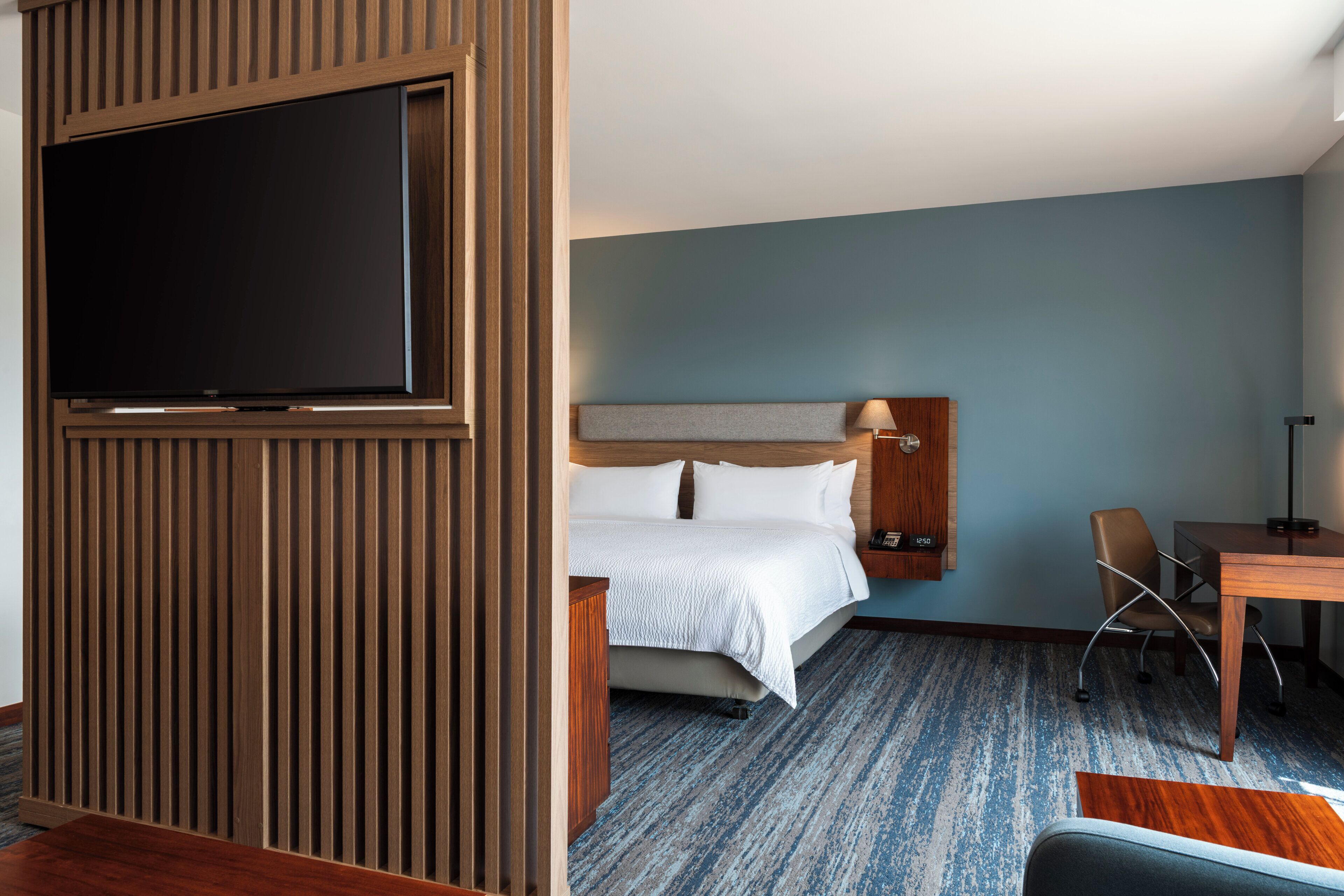 Quarto de hotel com cama, escrivaninha, cadeira, televisão e televisão montada na parede.