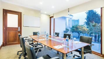 A conference room with a long table, chairs, a whiteboard, and a view of buildings and trees through large windows.