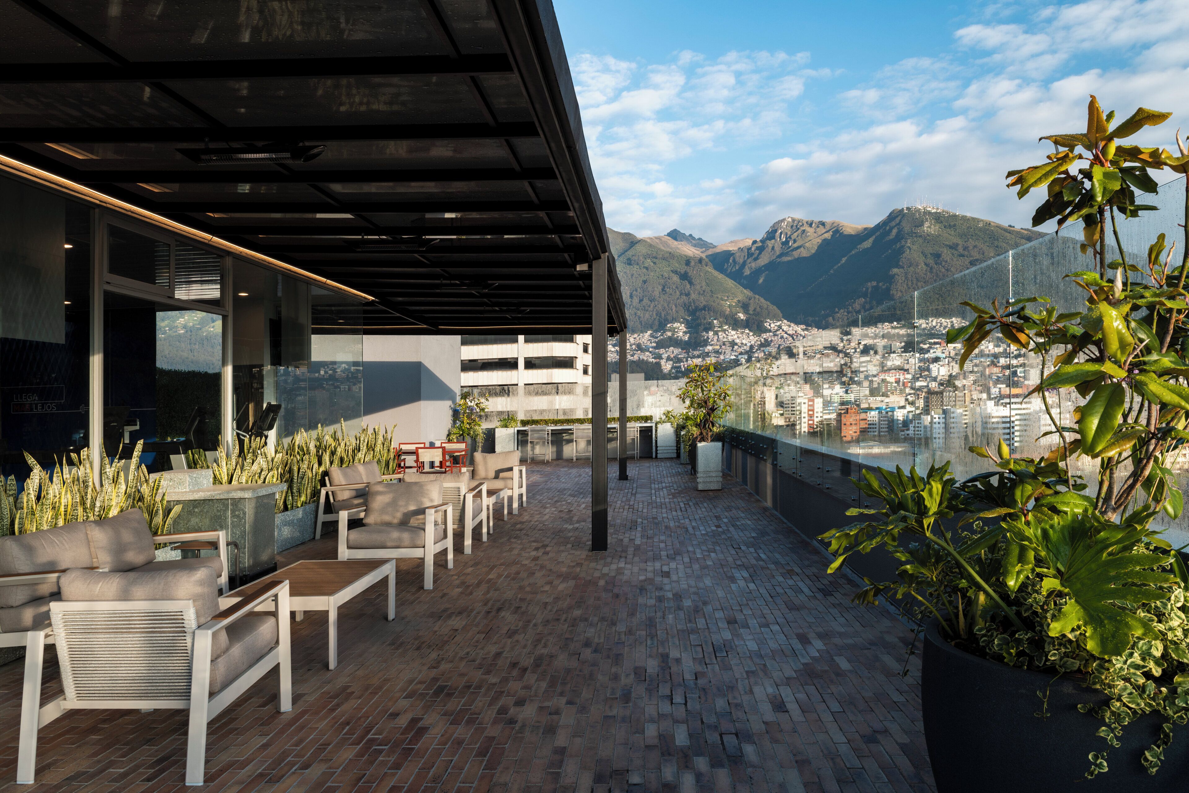 A rooftop terrace with outdoor seating, a view of a cityscape, and mountains in the background.