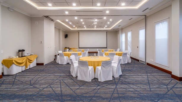A conference room with multiple round tables, white chairs, and a projector screen. - Holiday Inn Express Quito by IHG (Quito)