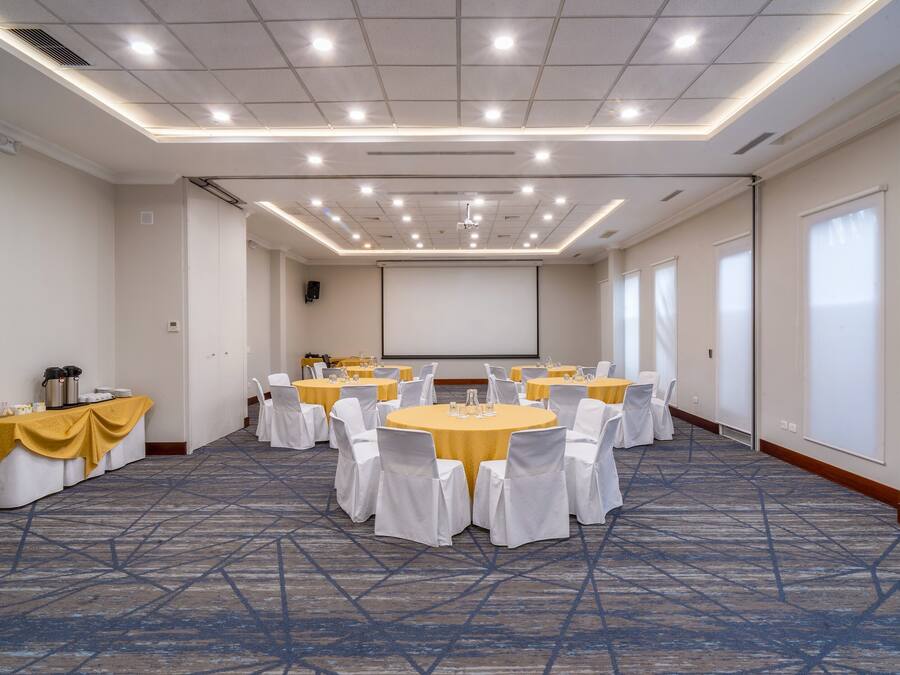 A conference room with multiple round tables, white chairs, and a projector screen.