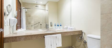 A modern bathroom with a granite countertop, a large mirror, a shower, and a toilet.