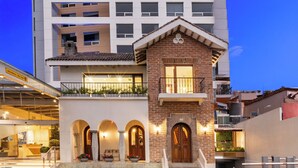 Un hotel con fachada de ladrillo, entrada abovedada y un balcón en el segundo piso con plantas.