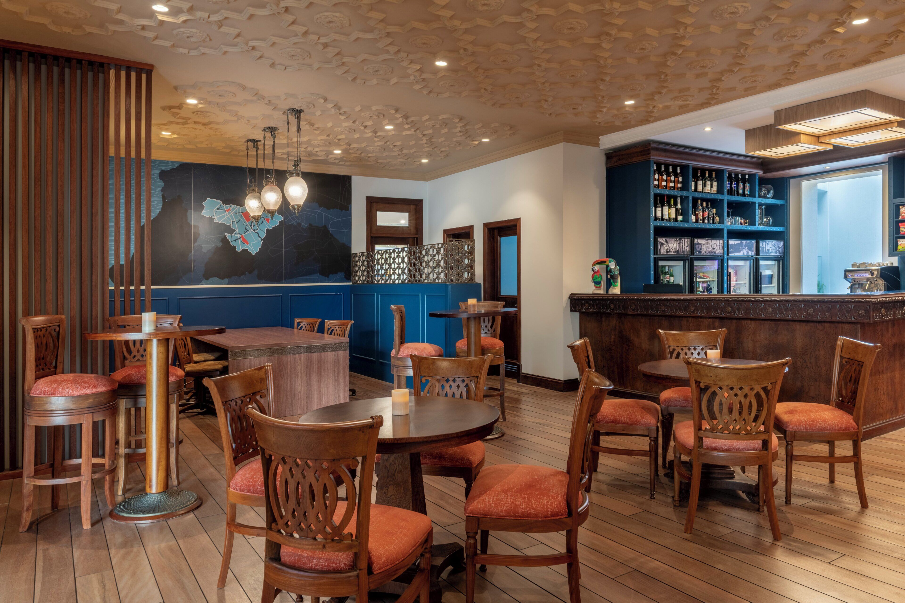 A restaurant with wooden tables and chairs, a bar area with shelves of bottles, and a decorative ceiling.