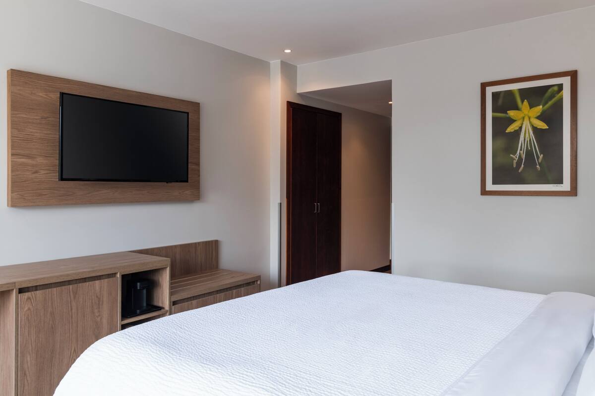 Habitació d'hotel moderna amb un llit gran, un televisor de pantalla plana muntat sobre un panell de fusta, una màquina de cafè i un quadre al mur.