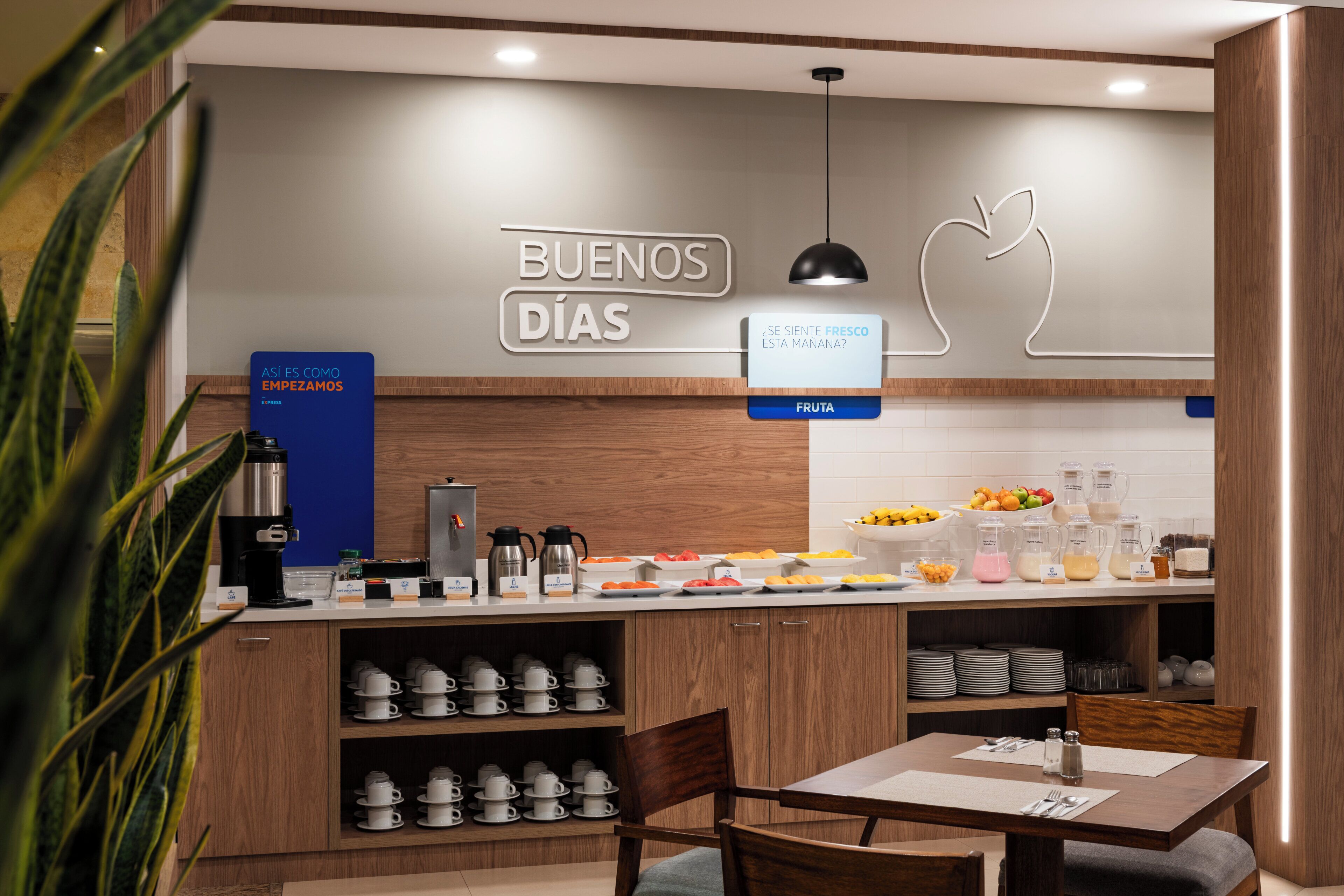 A modern breakfast area with a coffee station, fruit display, and seating.