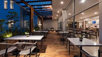 An outdoor dining area with tables and chairs, a brick floor, and a pergola structure.