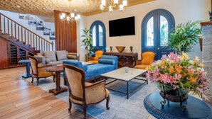 Un amplio salón con una escalera de madera, sofás azules y un gran arreglo floral.