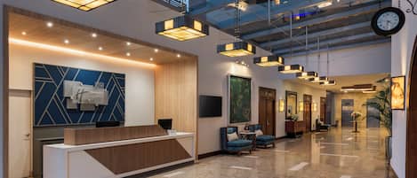 A modern hotel lobby with a reception desk, seating area, and a large glass ceiling.